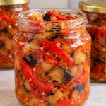 Салата от печени чушки и патладжан за зимата в буркани Tri burkana s domashna salata ot pecheni chushki i patladzhan za zimata, s vidimi parcheta cherveni chushki, patladzhan i luk, kato predniyat burkan e otvoren.